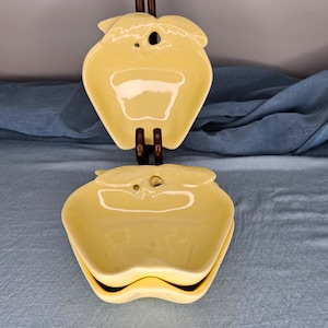 May include: Two yellow ceramic apple-shaped serving dishes. The dishes are stacked on top of each other.