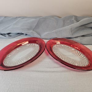 May include: Two oval-shaped glass serving dishes with a raised, textured pattern. The dishes are a deep red color with a clear glass center.