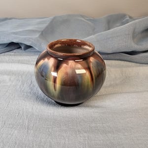 May include: A brown ceramic vase with a mottled glaze in shades of blue, green, and yellow. The vase has a rounded shape and a smooth, glossy finish.