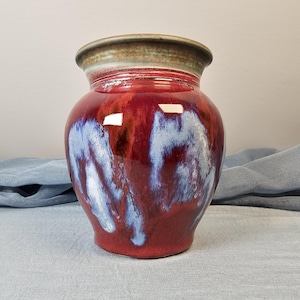 May include: A red and white ceramic vase with a rounded body and a flared rim. The vase has a mottled glaze with shades of red, white, and blue.