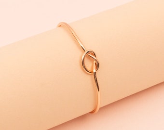 Peut inclure: Un bracelet jonc doré avec un motif de nœud. Ce bijou simple et élégant est un accessoire polyvalent. Le nœud est le point central du design, ajoutant une touche d'intérêt au style minimaliste.