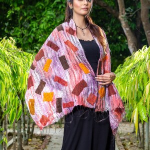 May include: A woman wearing a black dress and a colorful patterned scarf with brown, orange, and pink accents. The scarf is draped over her shoulders and tied at her neck.