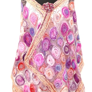 May include: A sheer, white shawl adorned with numerous felted rose designs in shades of pink, purple, and red. The shawl features a decorative border and is secured with a matching flower pin at the neckline. The shawl is draped over a mannequin.