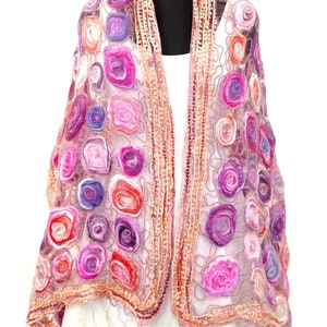 May include: A sheer, open-front shawl with a floral design. The shawl features a variety of colorful, spiral-shaped flowers in shades of pink, purple, and red. The edges are trimmed with a textured, light brown border.