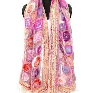 May include: A sheer, pink scarf with a floral pattern in shades of red, pink, and purple. The scarf has a delicate, open weave and is trimmed with a textured border and fringe.