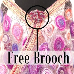 May include: A decorative shawl with a floral design in shades of pink, purple, and orange. The shawl is adorned with a free brooch at the neckline. The brooch is a small, flower-shaped accessory with red and gray accents.