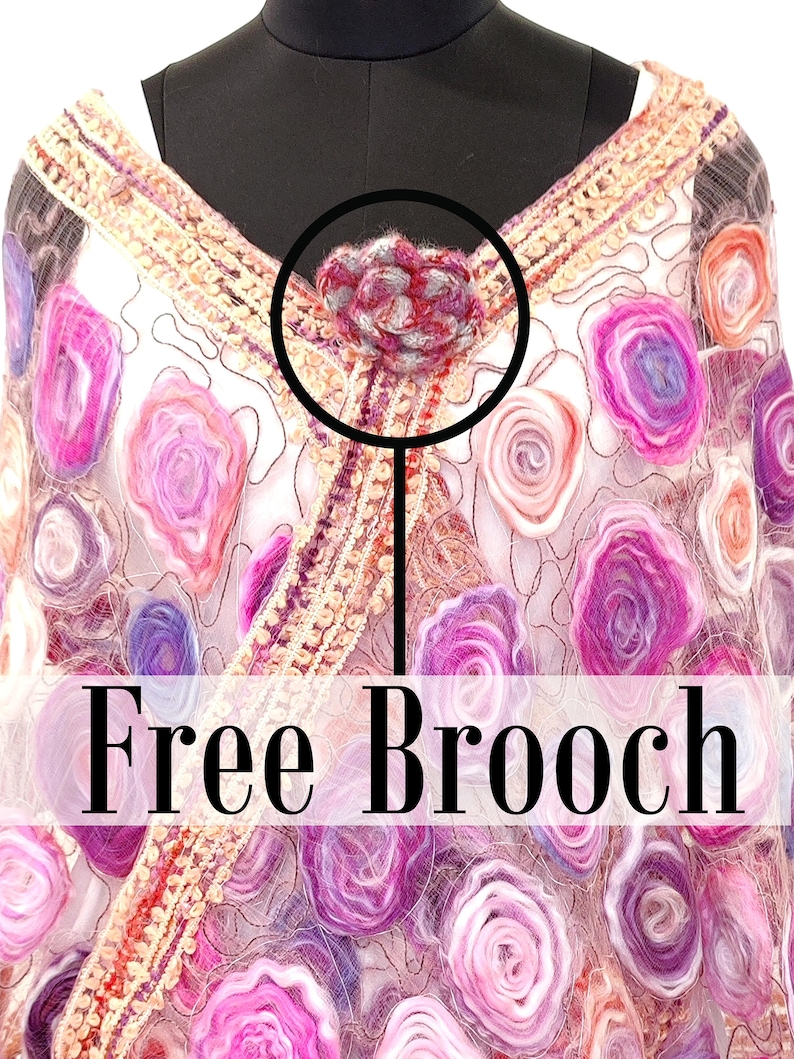 May include: A decorative shawl with a floral design in shades of pink, purple, and orange. The shawl is adorned with a free brooch at the neckline. The brooch is a small, flower-shaped accessory with red and gray accents.