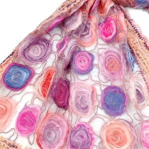 May include: A close-up of a sheer, floral-patterned scarf. The scarf features a delicate net base with colorful, textured, circular flower designs in shades of pink, purple, and orange. The edges are trimmed with a crocheted border.