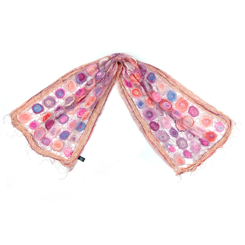 May include: A delicate, open-weave scarf featuring a pattern of colorful, spiral-shaped embellishments. The scarf showcases a palette of pinks, purples, and blues, with a fringed edge. The scarf is made of a soft, lightweight material.