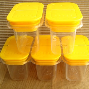 May include: Six yellow plastic spice jars with clear glass containers. The jars are stacked in pairs, with the lids facing up.