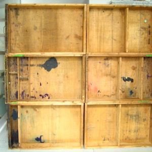 Op de afbeelding: Een stapel van zes open houten laden, elk met een rechthoekige vorm en een natuurlijke houten afwerking. De laden vertonen tekenen van ouderdom met donkere vlekken en verfspatten. Sommige laden hebben interne verdelers.