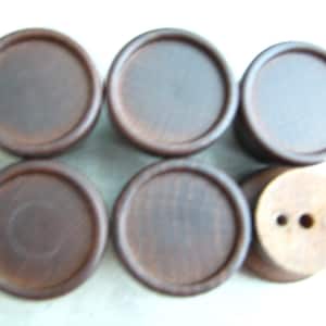 Könnte beinhalten: Sechs dunkelbraune Holzuntersetzer. Fünf sind flach mit erhabenem Rand, und einer hat drei Löcher. Die Untersetzer sind in zwei Reihen zu je drei angeordnet.