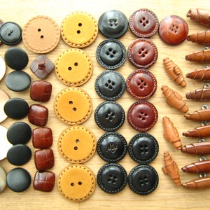 Puede incluir: Surtido de botones en varios colores, materiales y tamaños, incluyendo marrón, negro, beige y blanco. Algunos botones tienen una superficie texturizada, mientras que otros son lisos. También hay varios botones de madera en color marrón y beige.