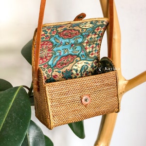May include: A small, rectangular rattan bag with a brown leather strap and a floral patterned fabric lining. The bag is open and the lining is visible.