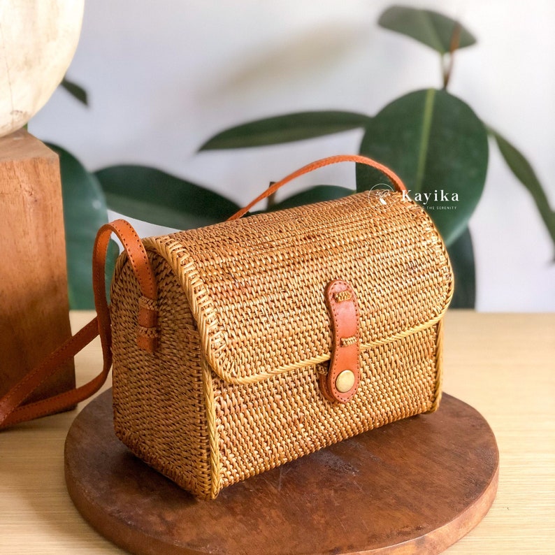 May include: A small, rectangular woven bag with a brown leather strap and a brass buckle. The bag is made of natural materials and has a rustic, earthy look.