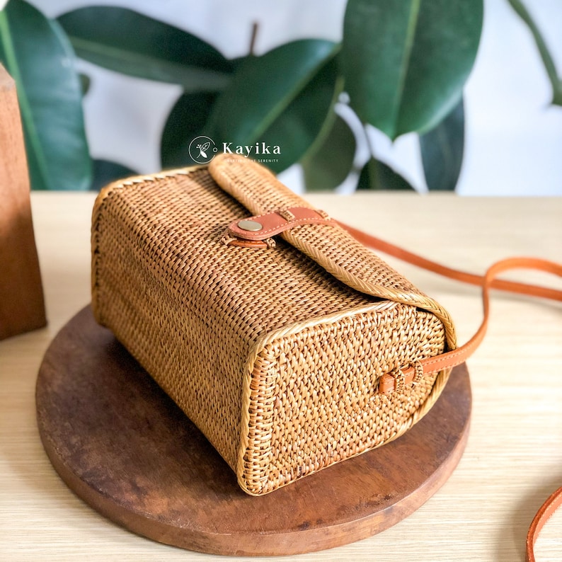 May include: A woven straw crossbody bag with a brown leather strap and a flap closure. The bag has a rectangular shape and a woven texture.