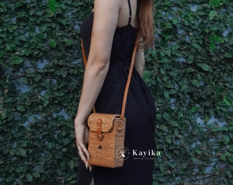 Könnte beinhalten: Eine Frau trägt ein schwarzes Kleid mit einer braunen geflochtenen Umhängetasche. Die Tasche hat einen Klappverschluss und einen Lederriemen. Die Tasche wird von Kayika hergestellt, Crafting the Serenity.