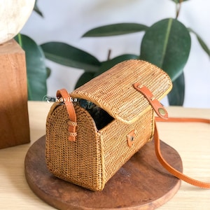 May include: A brown woven crossbody bag with a leather strap and a flap closure. The bag is open and the inside is lined with a blue and white fabric.