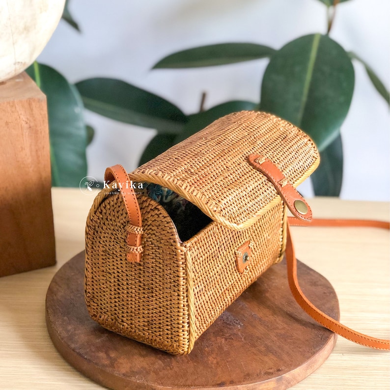 May include: A brown woven crossbody bag with a leather strap and a flap closure. The bag is open and the inside is lined with a blue and white fabric.