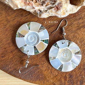 May include: A pair of silver earrings with a round, white, and green abalone shell design. The shell is made up of many small pieces of abalone shell, and the design is a spiral. The earrings are hanging from silver hooks.