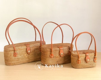 Könnte beinhalten: Drei geflochtene Rattan-Handtaschen mit braunen Ledergriffen und Messingakzenten. Die Taschen sind in verschiedenen Größen und von der größten bis zur kleinsten angeordnet.