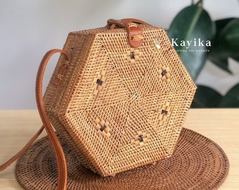 May include: A hexagonal woven rattan bag with a brown leather strap. The bag has a geometric pattern and is made of natural materials.