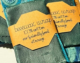 May include: A stack of green and blue beeswax food wraps with a brown label that reads "beeswax wrap 100% cotton eco-friendly food storage" and another label that reads "wax wrap 0% cotton friendly food storage".