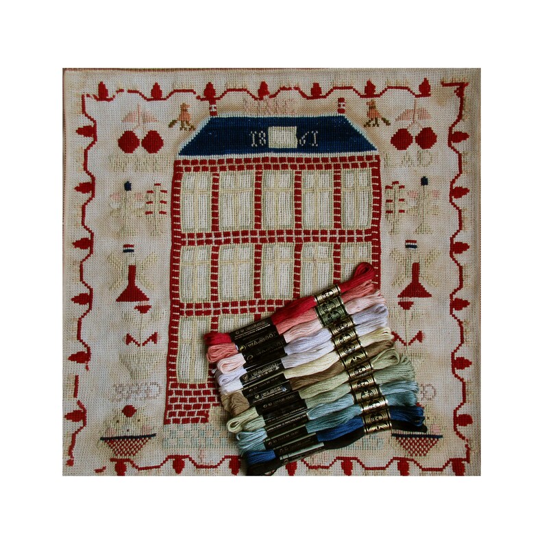 May include: A vintage needlepoint sampler featuring a red brick house with a blue roof and a white door. The house has 1861 written above the door. The sampler is surrounded by a red and white border with a floral design. A stack of embroidery floss in various colors is in the bottom right corner of the image.
