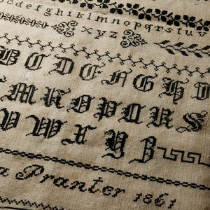 May include: Black and white sampler with a cross-stitch alphabet and the text "a Pranter 1861".