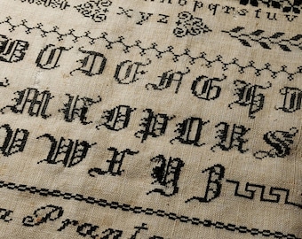 Peut inclure: Broderie au point de croix en noir et blanc avec un alphabet et le texte "a Pranter 1861".