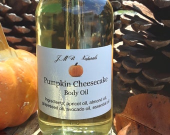 Puede incluir: Una botella de vidrio de aceite corporal de pastel de queso de calabaza de JMB Naturals. La botella tiene un gotero y está sobre una superficie de madera con una piña y una pequeña calabaza naranja.