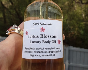 以下が含まれることがあります： 黒いドロッパー付きの透明なガラス瓶と白いラベル。ラベルには「JMB Naturals Lotus Blossom Luxury Body Oil」と、成分としてアプリコットカーネルオイル、スイートアーモンドオイル、アボカドオイル、グレープシードオイル、フレグランス、エッセンシャルオイルが記載されています。
