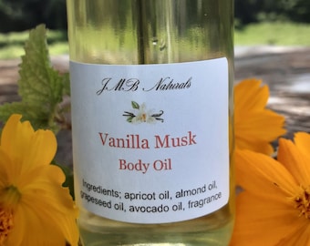 May include: A clear glass bottle with a black lid, labeled "JMB Naturals Vanilla Musk Body Oil". The label lists ingredients: apricot oil, almond oil, grapeseed oil, avocado oil, and fragrance.