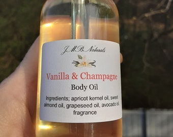 May include: A clear glass bottle with a black dropper top filled with a light yellow liquid. The bottle has a white label with the text "JMB Naturals Vanilla & Champagne Body Oil" and a list of ingredients.