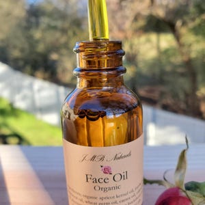 May include: A brown glass bottle with a dropper filled with a yellow liquid. The bottle has a label that reads "JMB Naturals Face Oil Organic" and lists the ingredients: organic apricot kernel oil, jojoba oil, wheat germ oil, carrot oil, Himalayan oil, rosehip oil, sea buckthorn oil, frankincense oil, rose oil & essential oils.