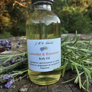 May include: A clear glass bottle with a black dropper top filled with a light yellow liquid. The bottle has a white label with the text "JMB. Naturals Lavender & Rosemary Body Oil" and a list of ingredients: apricot kernel oil, sweet almond oil, grapeseed oil, avocado oil, and fragrance.