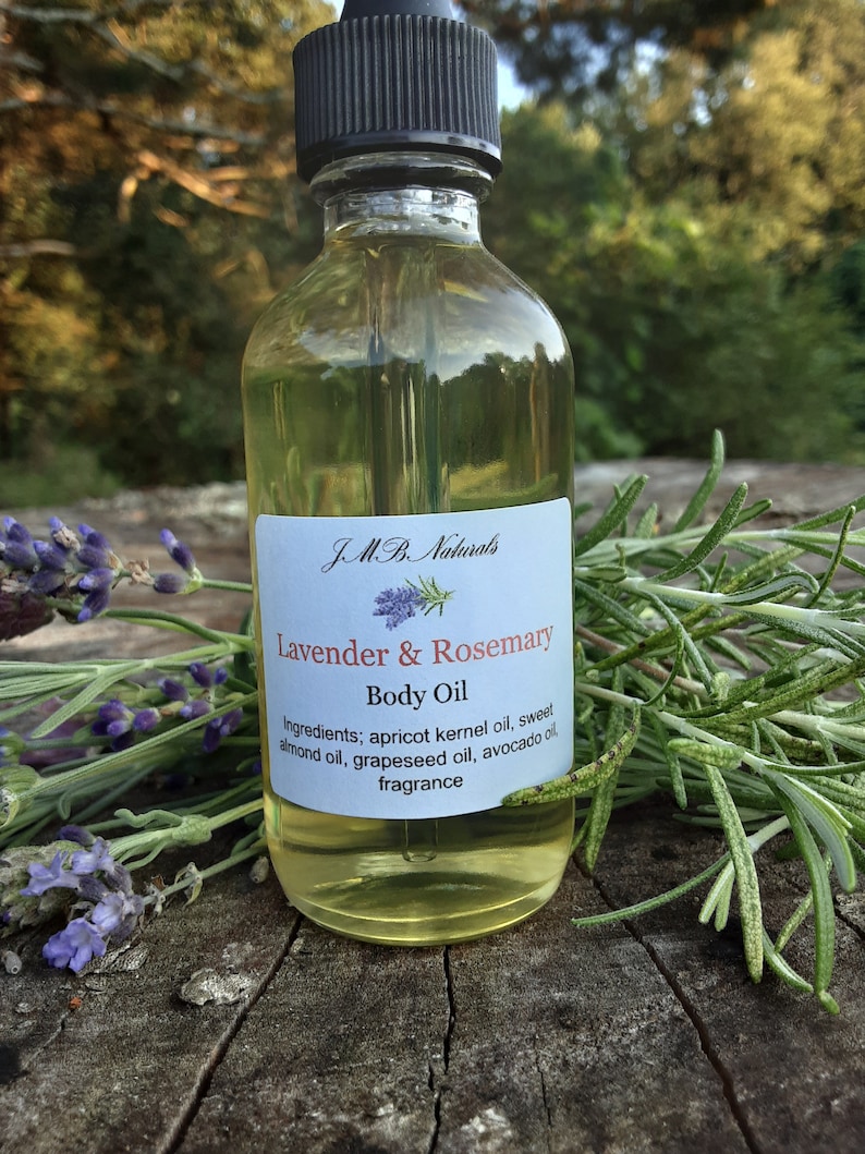 May include: A clear glass bottle with a black dropper top filled with a light yellow liquid. The bottle has a white label with the text "JMB. Naturals Lavender & Rosemary Body Oil" and a list of ingredients: apricot kernel oil, sweet almond oil, grapeseed oil, avocado oil, and fragrance.