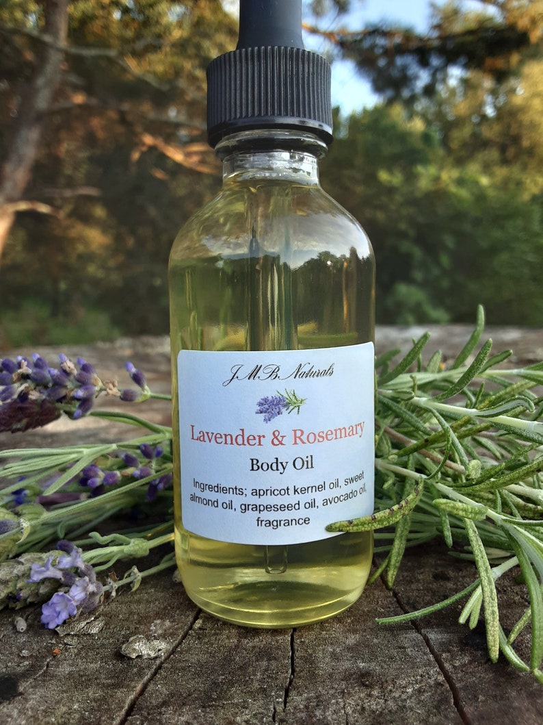 May include: A clear glass bottle with a black dropper top filled with a light yellow liquid. The bottle has a white label with the text "JMB Naturals Lavender & Rosemary Body Oil" and a list of ingredients.