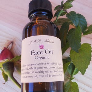 May include: A brown glass bottle with a dropper top and a white label that reads "JMB Naturals Face Oil Organic". The label lists the ingredients: organic apricot kernel oil, jojoba seed oil, wheat germ oil, carrot oil, calendula oil, Abyssinian oil, rosehip oil, sea buckthorn oil, frankincense oil, rose oil & essential oils.