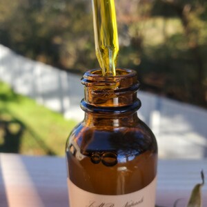 May include: A close-up of a brown glass bottle with a dropper filled with yellow liquid. The bottle is labeled "Face Oil Organic" with a pink rose graphic.