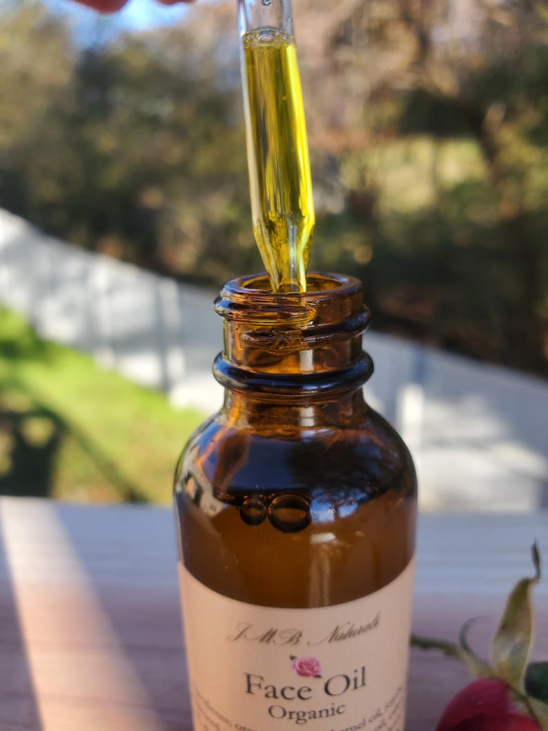May include: A close-up of a brown glass bottle with a dropper filled with yellow liquid. The bottle is labeled "Face Oil Organic" with a pink rose graphic.