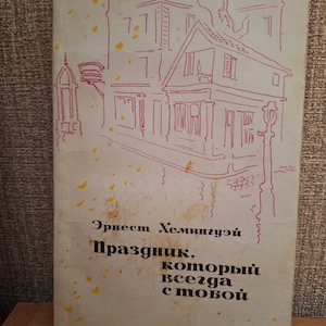Op de afbeelding: Vintage boekomslag met een roze lijntekening van gebouwen en een straatlantaarn. De titel en de naam van de auteur staan in het Russisch. De omslag heeft een versleten, verouderde uitstraling met gele vlekken.