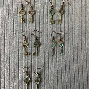 May include: Six pairs of antique key-shaped earrings with a bronze finish. The keys have intricate details and are suspended from silver hooks.