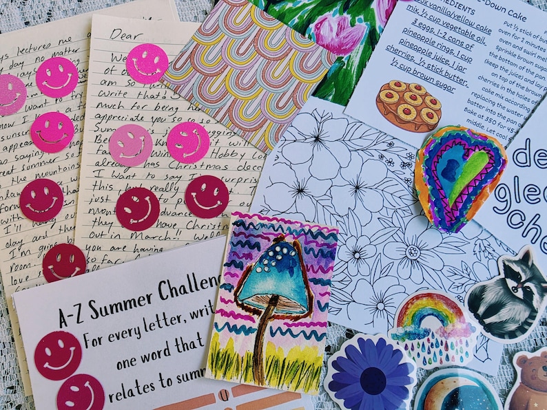 May include: A collection of stationery items including handwritten letters with pink smiley face stickers, a recipe card for pineapple upside-down cake, a rainbow pattern square, a floral coloring sheet, a watercolor mushroom, and various stickers.