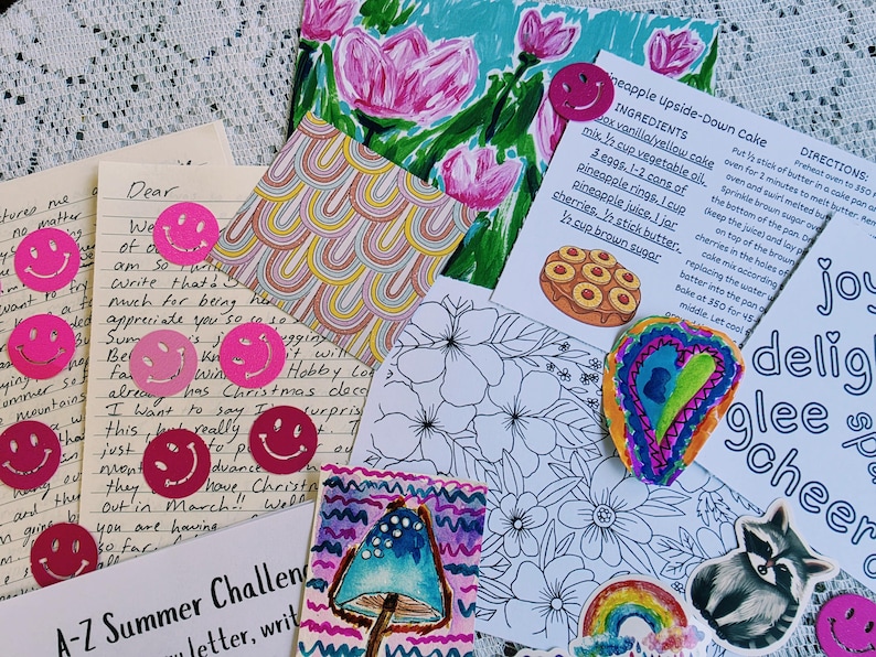 May include: A collection of stationery items including a handwritten letter, a recipe card for pineapple upside-down cake, a floral coloring page, a mushroom illustration, a raccoon sticker, and several small pink smiley face stickers.