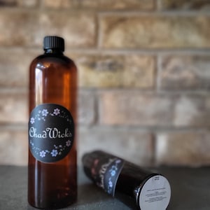May include: Two brown glass bottles with black lids. The larger bottle has a black and white label with the text "Chad Wicks" and a floral design. The smaller bottle has a black and white label with the text "Chad Wicks" and a floral design. The smaller bottle has a white label with text about the product.