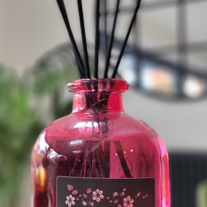 May include: A pink glass bottle with black reeds and a black label that reads "Chad Wick's Hand Poured Reed Diffuser - Pink Pepper - ".