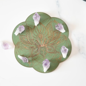 Könnte beinhalten: Ein grünes, kreisförmiges Mandala mit einem Lotusblumenmuster und goldenen Akzenten. Sechs Amethystkristalle sind auf dem Mandala platziert.