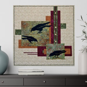 May include: A quilted wall hanging featuring three black crow silhouettes against a backdrop of geometric shapes in shades of brown, green, and burgundy. The background is a light beige with a diamond pattern. Decorative buttons accent a vertical stripe.