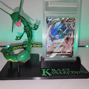 May include: A black plastic display stand with a green Rayquaza Pokemon figure and a graded Pokemon card featuring Rayquaza. The stand has the text "KRAZY KOLLECTIONS" printed on the front.